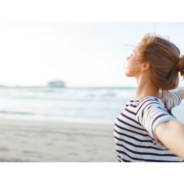 A woman stands by the ocean spreading her arms wide representing how to get unstuck when you're feeling trapped.