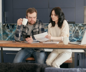 A couple looks stressed out as they look at some bills together. They need financial therapy for couples.