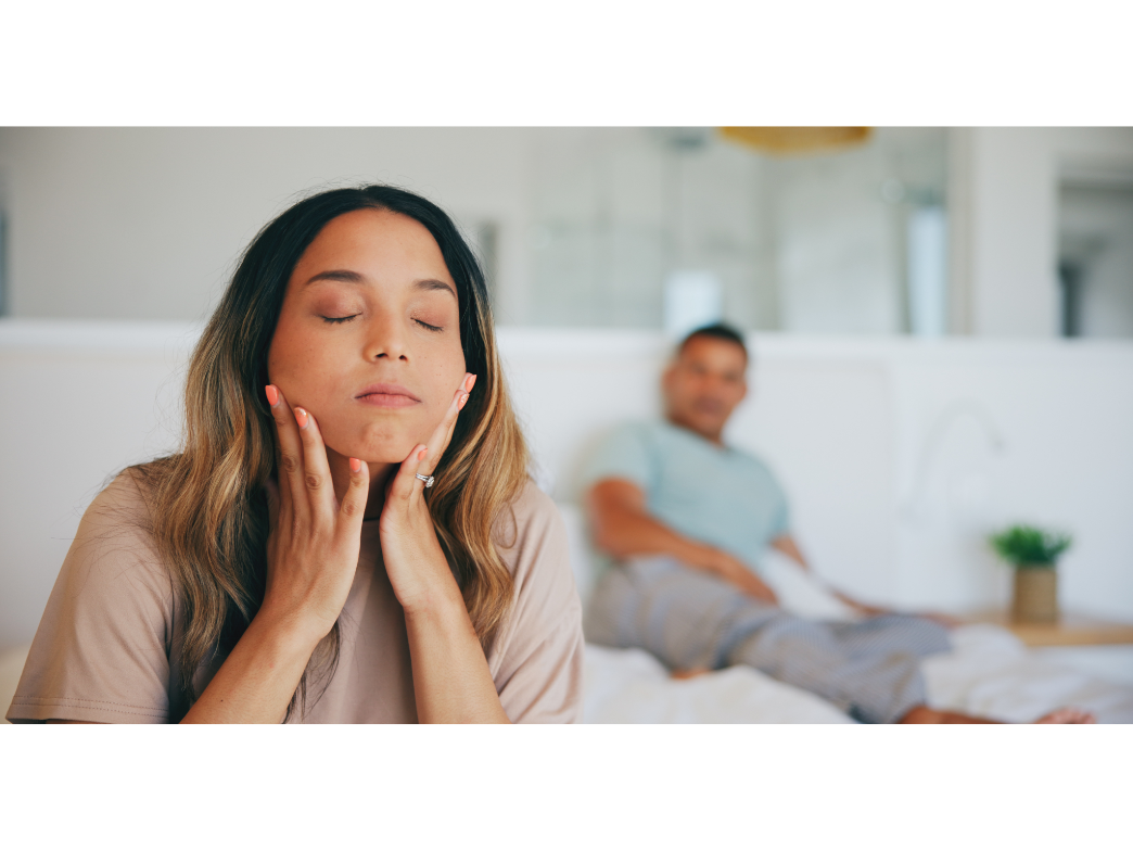 A woman looks frustrated sitting on the edge of the bed with a man out of focus in the background representing constantly arguing in a relationship