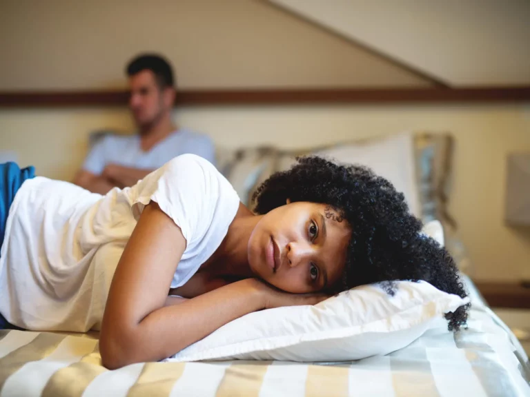woman lying on bed sad - man upset in back ground both wondering if we should breakup or stay together