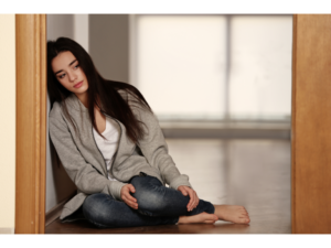 A woman sits on the floor looking sad representing the first step in recovering from a breakup, validation.