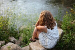 A woman sits on a rock and stares out at the water representing why you can't stop thinking about your Ex.