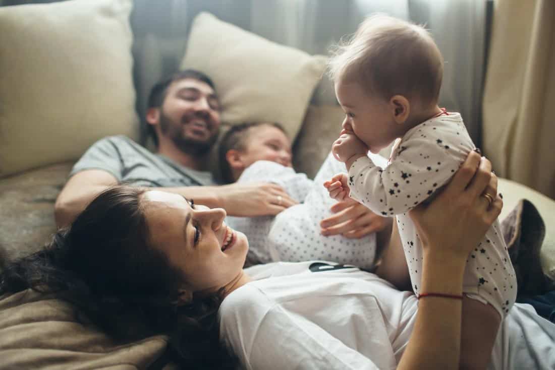 Family of a man, woman, toddler and baby lying in bed while father holds son and mother holds up baby.