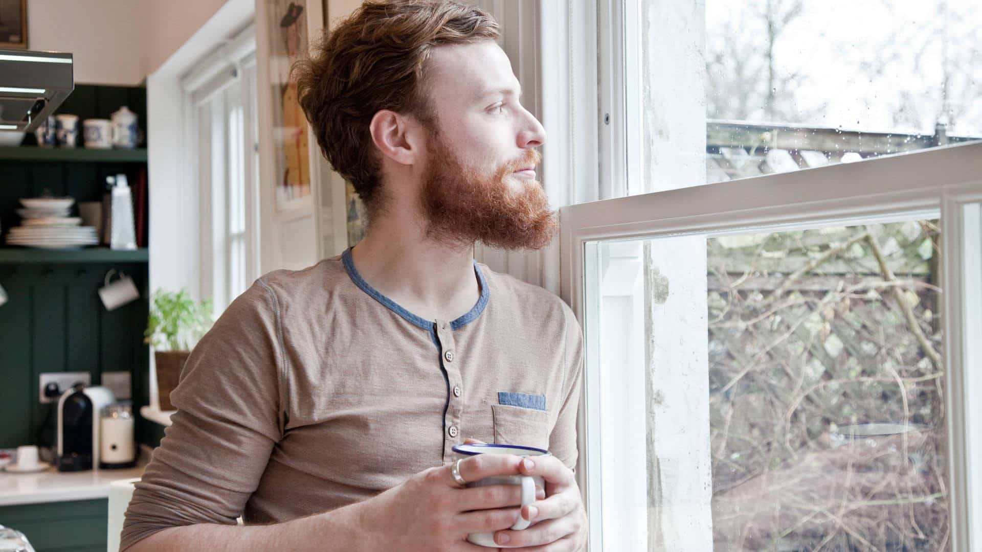 Man looking out of window with coffee mug, reflecting on Exaholics book