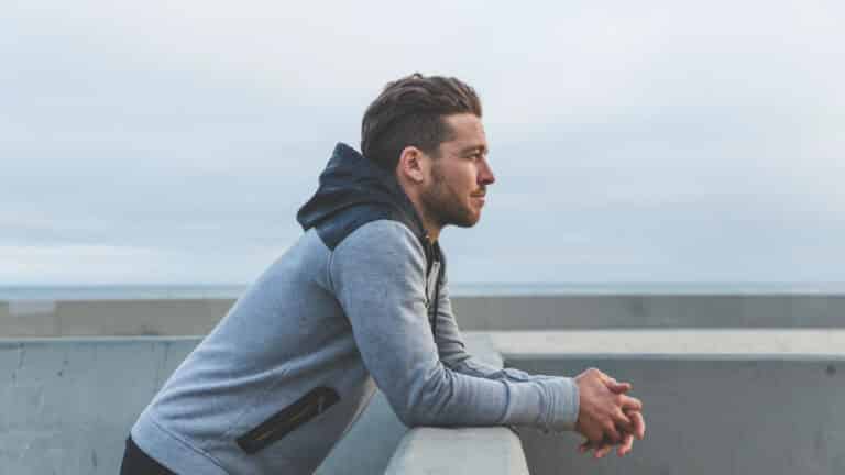 Man in thought leaning on railing of pier representing breakup coaching