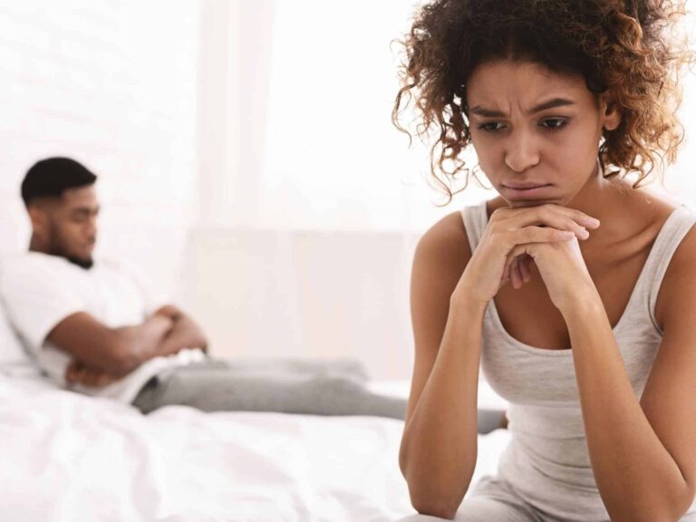 Anxious woman sits on the bed, feeling distant from her partner.