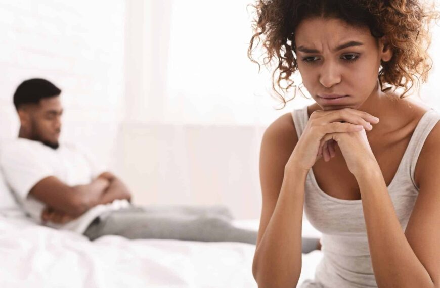 Anxious woman sits on the bed, feeling distant from her partner.