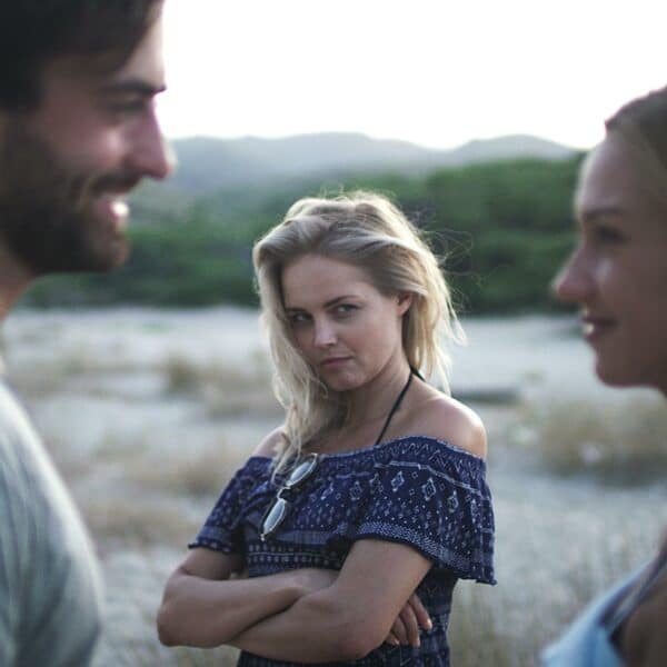 Is Jealousy Healthy In a Relationship? Jealous girlfriend scowling at boyfriend talking to another woman.