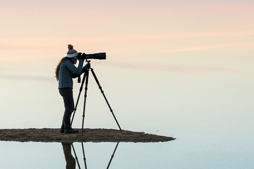 Photo of photographer on reflective water at dawn, representing career advice to achieve career clarity.