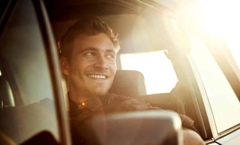 Happy young man on a road trip, smiling and looking out of car window