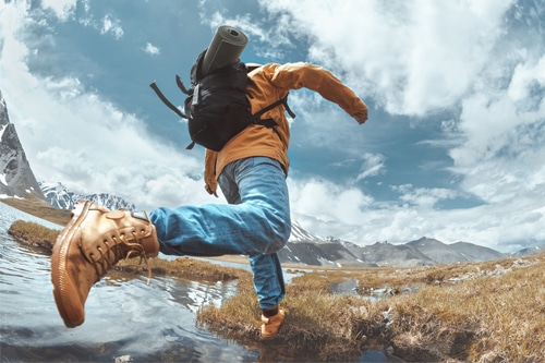 Photo of man hiking, boldly striding across stream. Represents advice for cultivating confidence and personal empowerment collection.