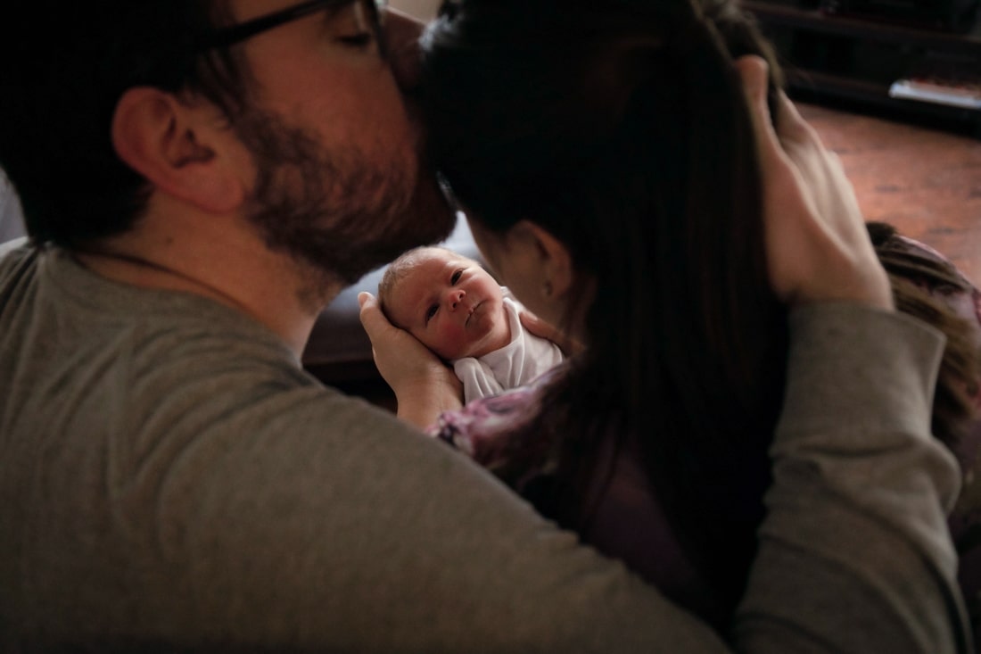 A father kissing his wife forehead as she looks at their newborn son