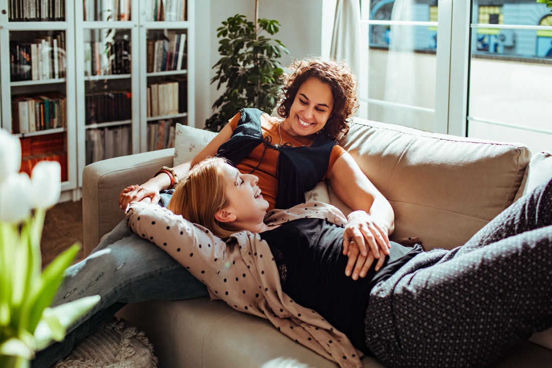 Female couple enjoying time together on a sofa, representing online couples counseling.