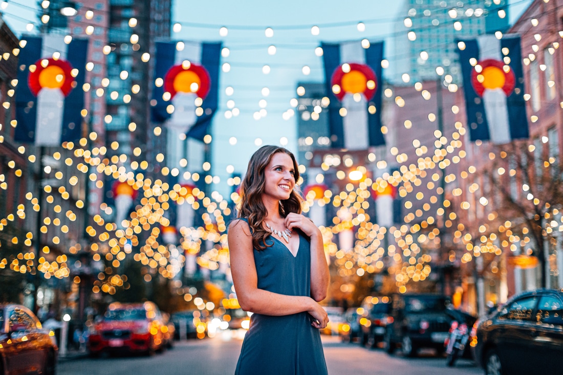 Embrace Happiness with Denver Life Coaching: Portrait of a Beautiful, Fashionable Young Woman Looking Up and Standing Under Colorado Flags and String Lights on Larimer Square in Denver, Colorado at Dusk