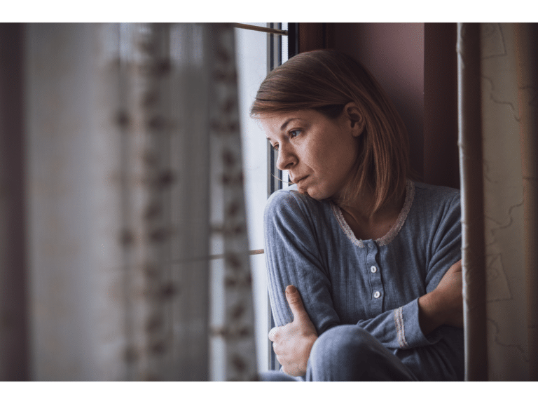 A woman looks out a window with a pained expression on her face representing betrayal trauma recovery