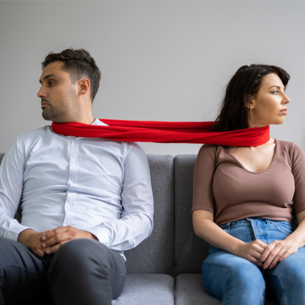 A couple sits on a couch with a red scarf around their necks, representing enmeshed relationships