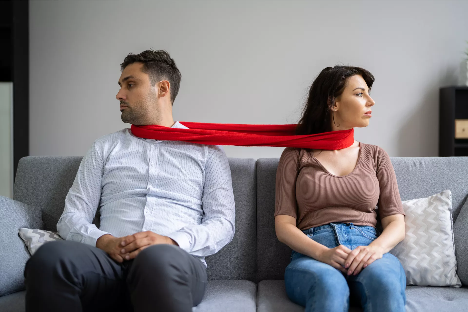 A couple sits on a couch with a red scarf around their necks, representing enmeshed relationships