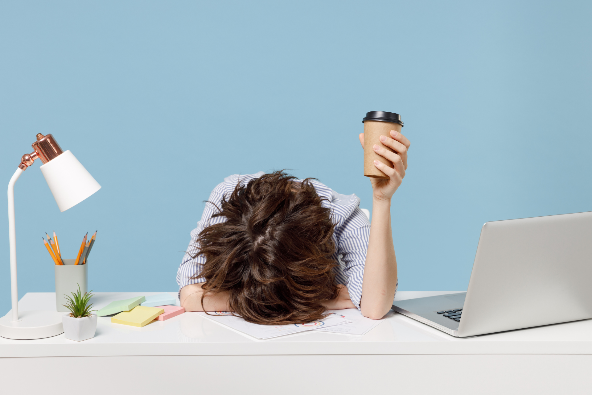 An overwhelmed woman puts her head down on her desk representing setting boundaries at work