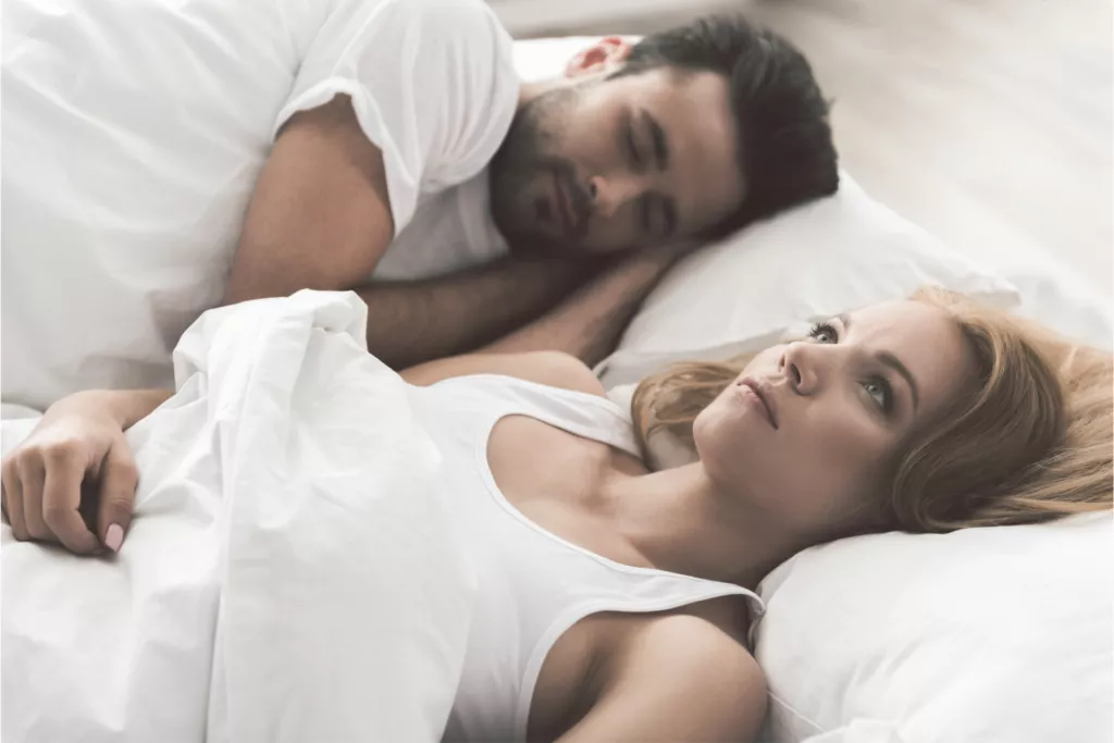 A woman lies in bed next to her partner representing why people fall out of love