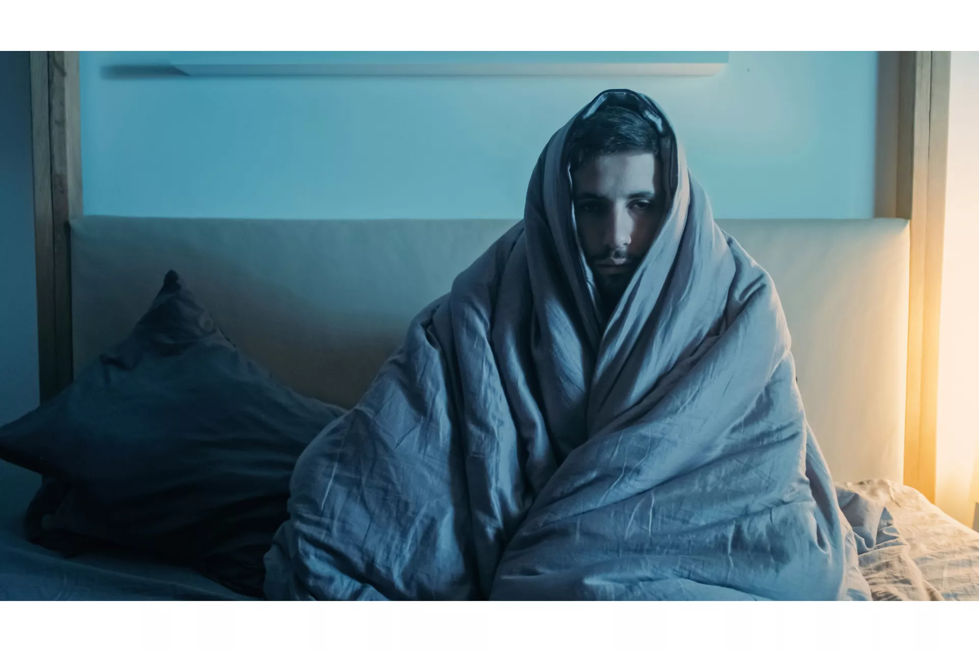 A man sits wrapped in a duvet representing how to stop overthinking after being cheated on