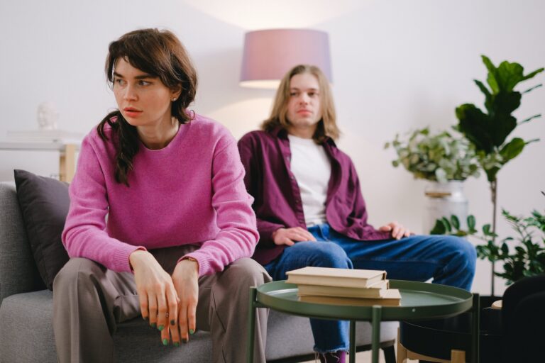 A man and a woman sit on the couch. They are angry and fighting representing a relationship surviving cheating.
