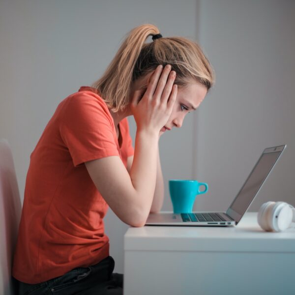 A woman works on her laptop at a desk. She has her head in her hands and looks unhappy signifying she's unmotivated at work.