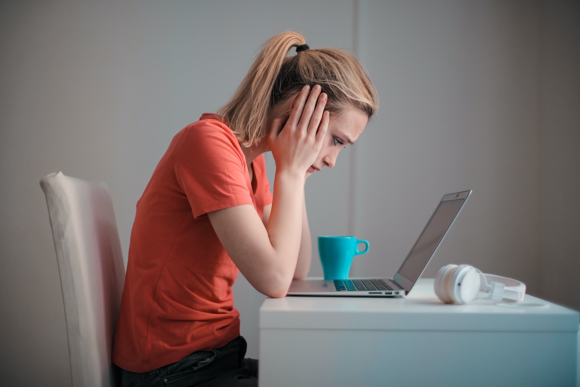 A woman works on her laptop at a desk. She has her head in her hands and looks unhappy signifying she's unmotivated at work.