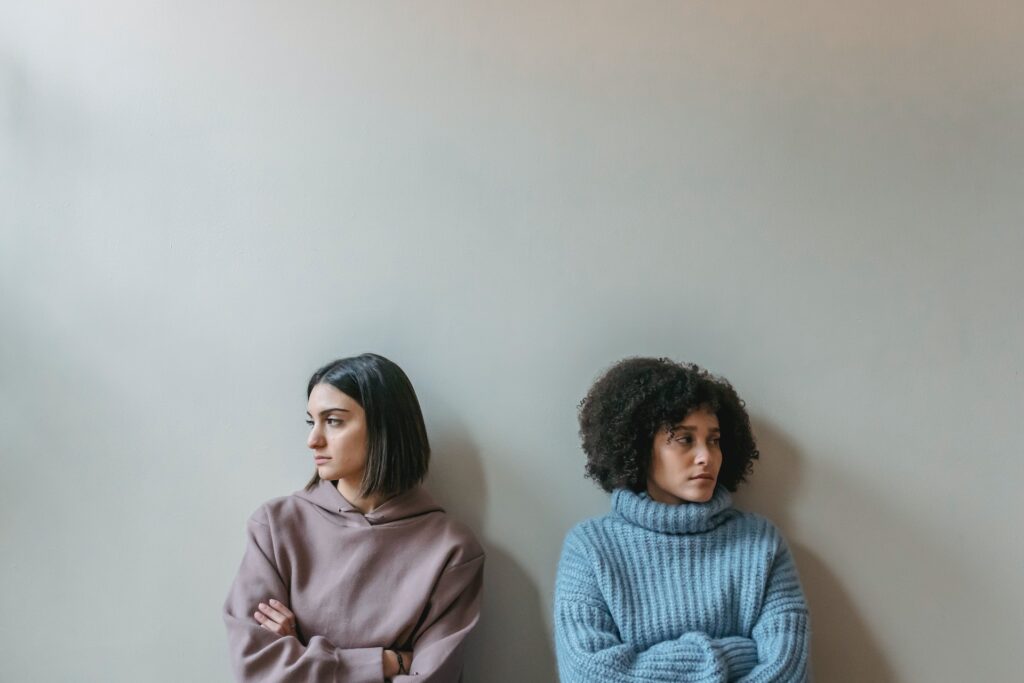 Two women stand against a wall with their arms crossed facing away from each other representing someone stepping over your boundaries.