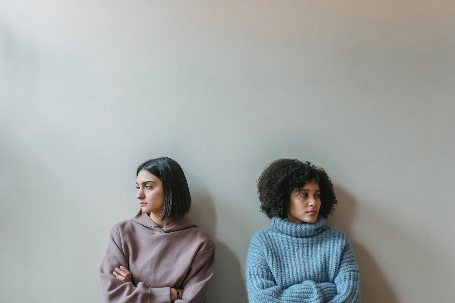 Two women stand against a wall with their arms crossed facing away from each other representing someone stepping over your boundaries.