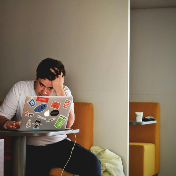 A man working on a laptop holds his head in his hands representing the signs of a toxic boss