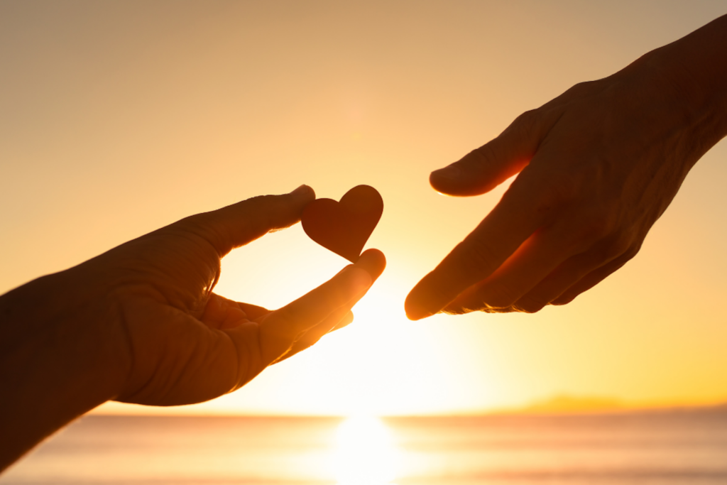 A hand reaches to give another hand a heart representing overgiving in relationships.