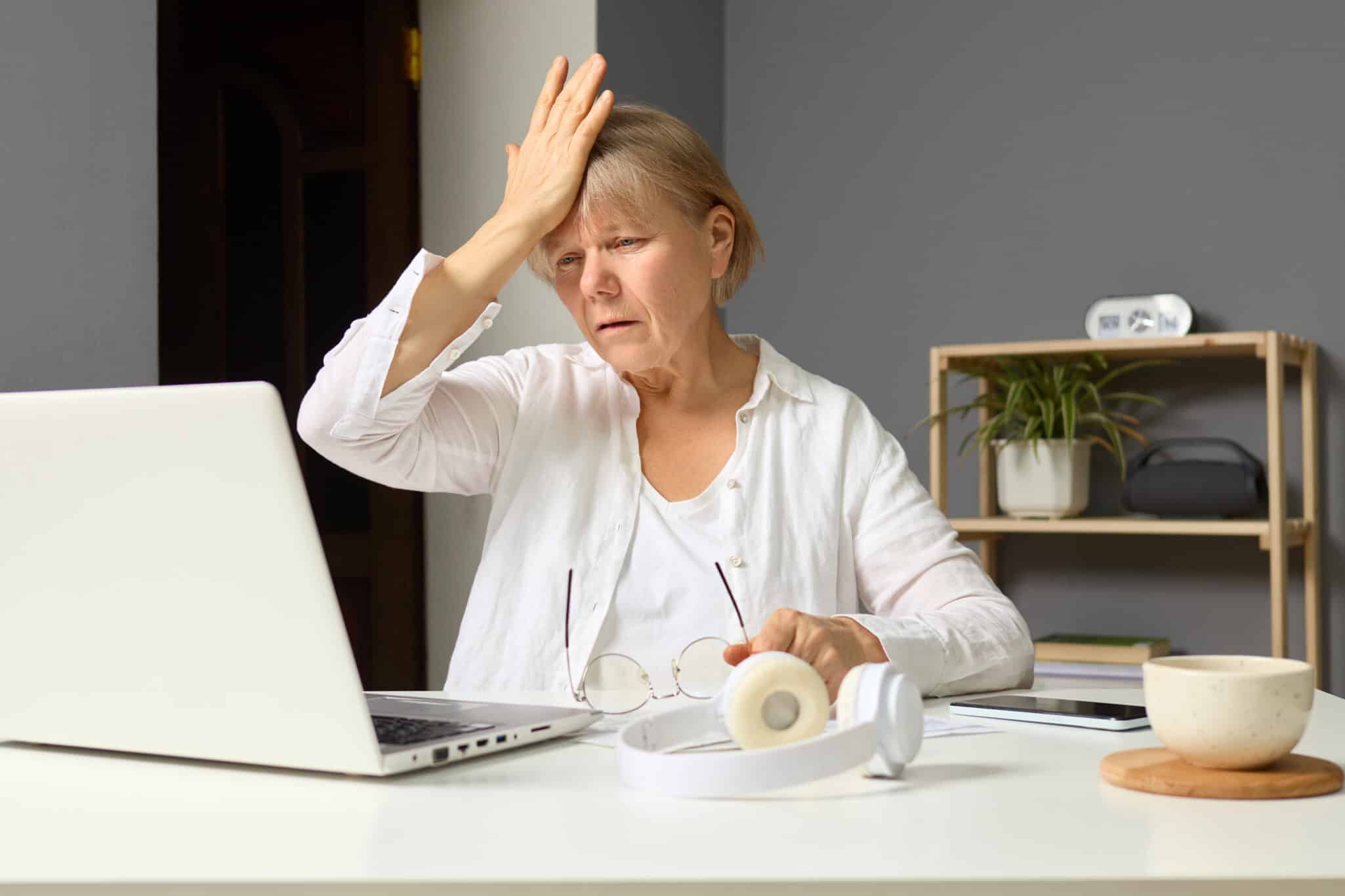 A therapist facepalms while sitting at her desk in front of her computer representing 5 common therapist mistakes that could derail your practice.
