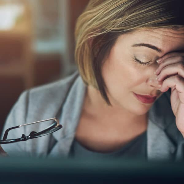A female therapist sits in front of her computer and holds her hand over her face representing how to avoid compassion fatigue with high intensity therapy clients.