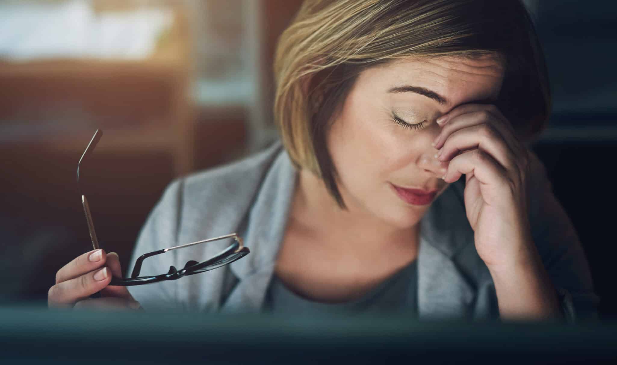 A female therapist sits in front of her computer and holds her hand over her face representing how to avoid compassion fatigue with high intensity therapy clients.