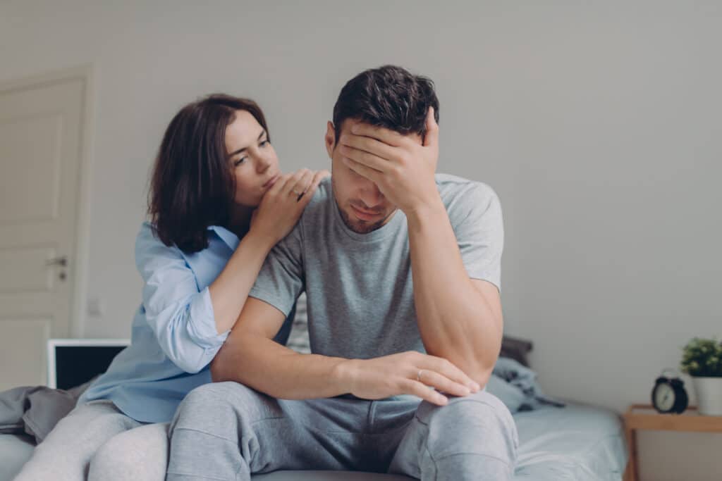A woman comforts her husband on the bed with a laptop next to them representing porn addiction recovery - how to recognize it and start the path to healing.