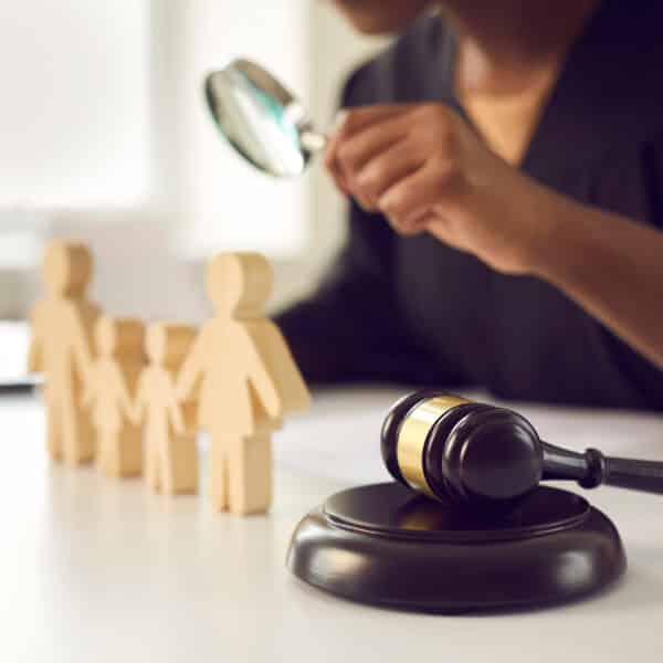 A CFI investigator looks through a magnifying glass at wooden figures depicting a family representing The Child and Family Investigation Process - What Every Therapist Needs to Know