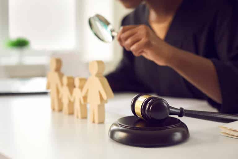 A CFI investigator looks through a magnifying glass at wooden figures depicting a family representing The Child and Family Investigation Process - What Every Therapist Needs to Know