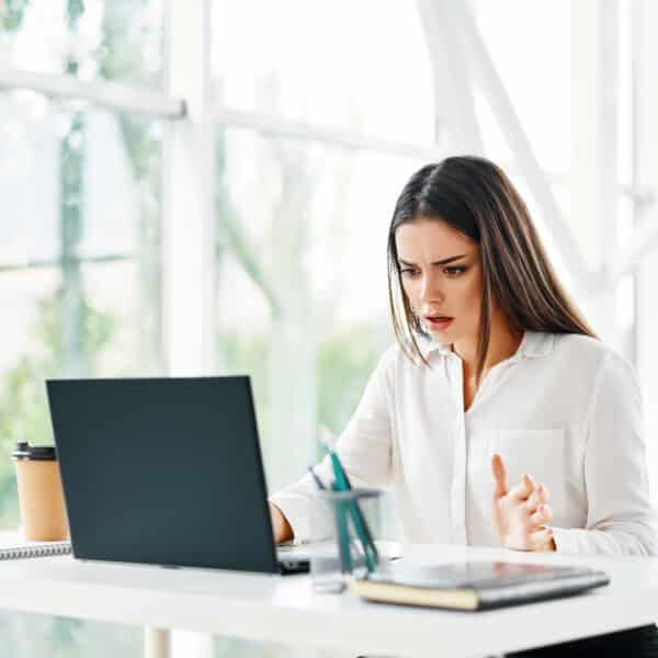 A therapist sits at his laptop with a warning sign hovering above the keyboard representing Is Your Mental Health EHR Sabotaging Your Therapy Practice?