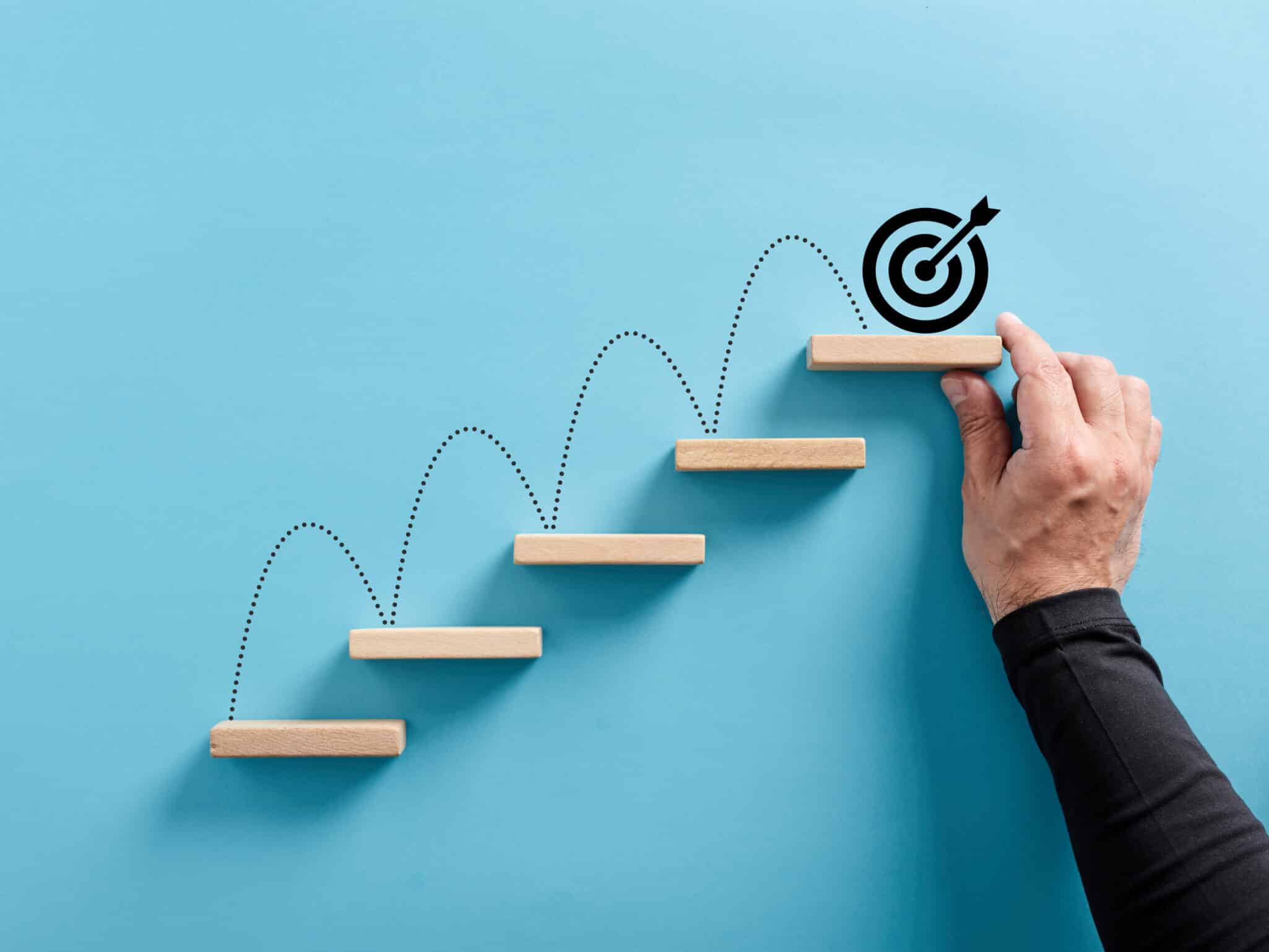 Wooden steps ascending with a target at the top representing Settings Goals for a Life and Career You Love as a Therapist.