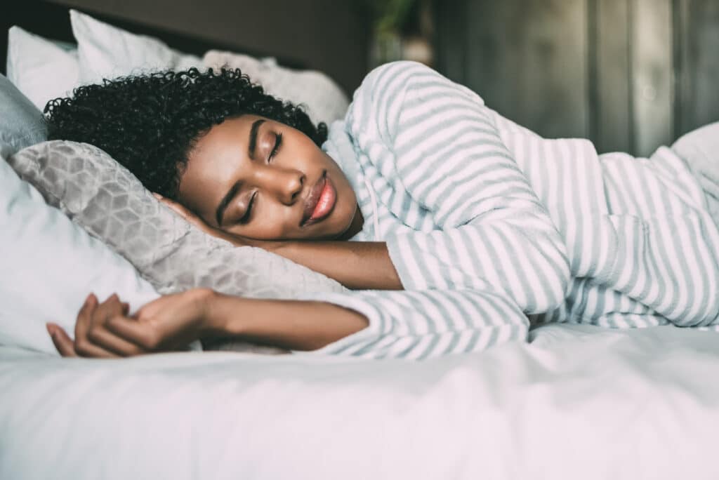 A close up of a pretty black woman sleeping in bed representing Your Sleep Helpline: Secrets for Better Nights and Brighter Days.