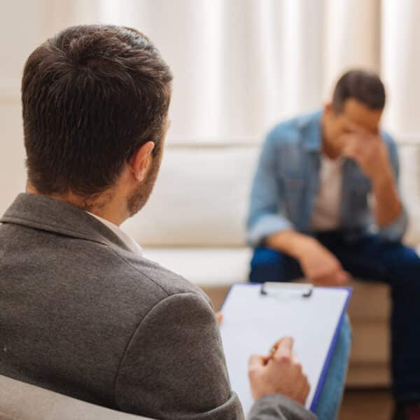 A man sits in therapy with his therapist and holds his head in his hands representing Help! My Client Says ‘Therapy Isn’t Working’—Now What?