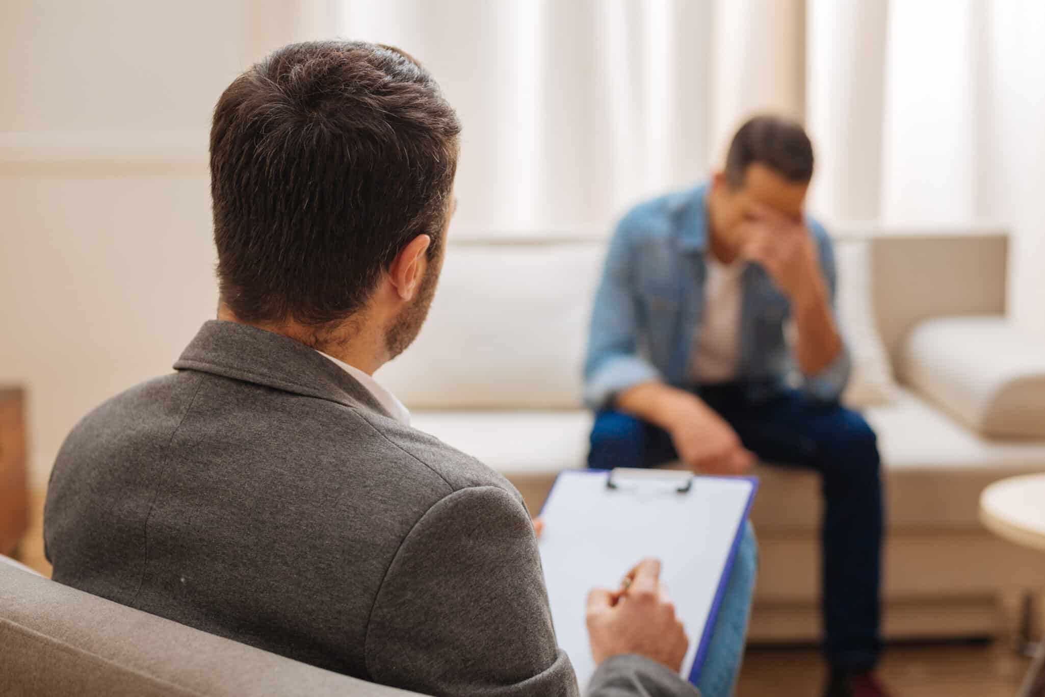 A man sits in therapy with his therapist and holds his head in his hands representing Help! My Client Says ‘Therapy Isn’t Working’—Now What?