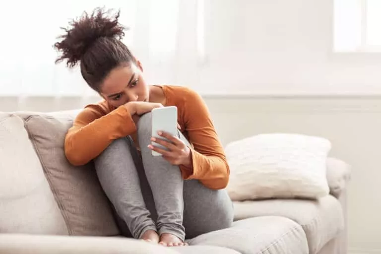 A woman sits on her couch looking at a photo of her ex on her cell phone representing why did my ex move on so fast?