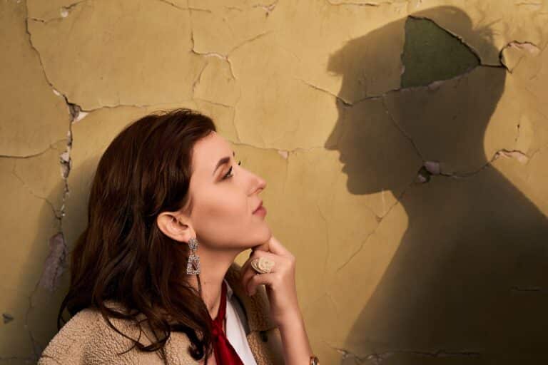 A woman stands against a wall facing a shadow of her ex representing why I do still think about my ex?