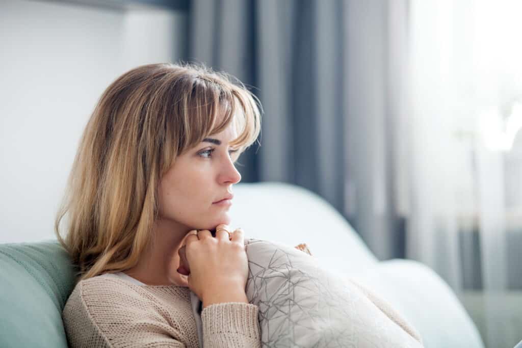 A sad woman sits on her couch after a breakup representing losing yourself in a relationship.