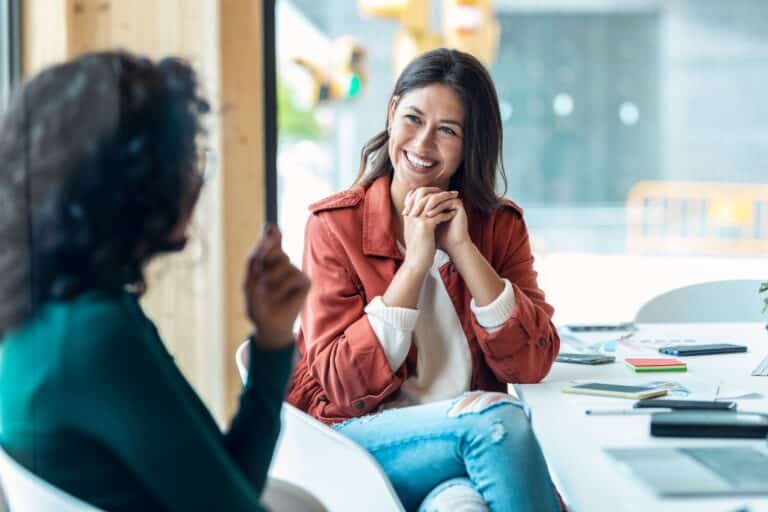 A happy woman talks with her life coach representing Why Therapy Clients Are Hiring Coaches (And Leaving Therapy Behind)
