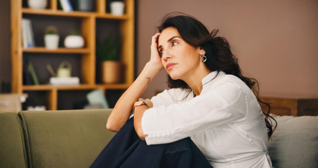 A woman sitting on her couch overthinking representing How to Stop Overthinking and Find Inner Peace