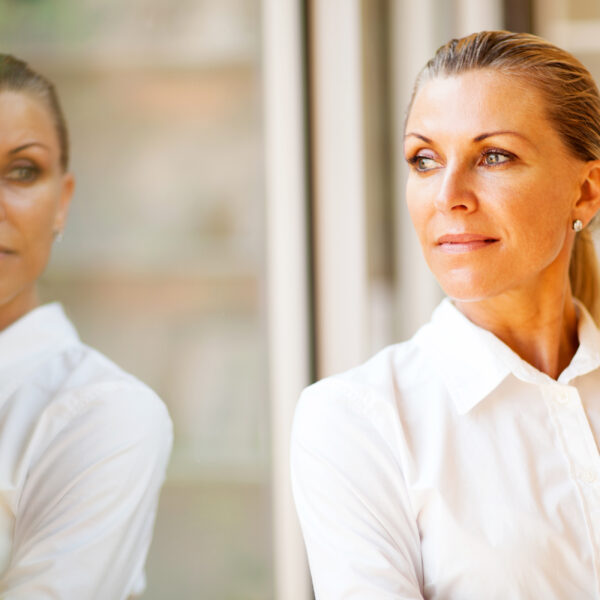 A woman looking at her reflection in a window representing Stuck in the “I Hate My Life” Spiral? It’s Time For a Hard Reset.