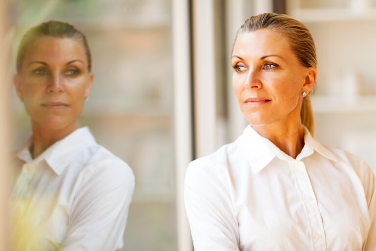 A woman looking at her reflection in a window representing Stuck in the “I Hate My Life” Spiral? It’s Time For a Hard Reset.