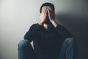 A man sits with his head in his hands representing What Are the Signs a Man Might Be Suffering in Silence?